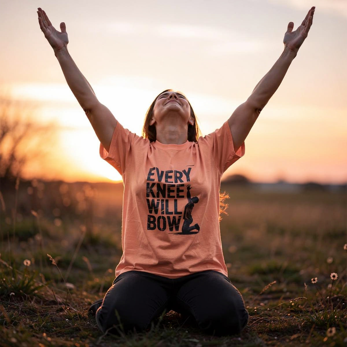 Person sitting in a field with arms raised wearing a t-shirt with a message.