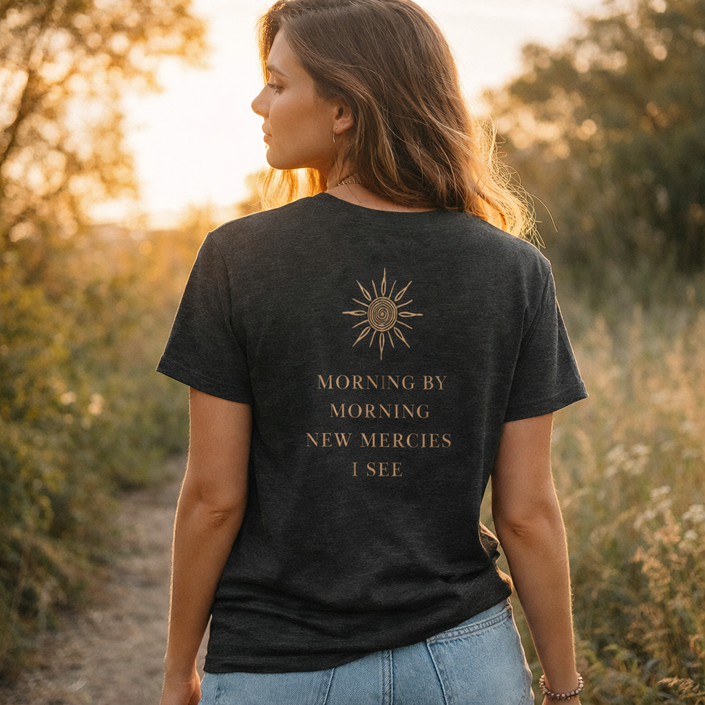 Woman wearing a black t-shirt with a sun design and text in a field at sunset