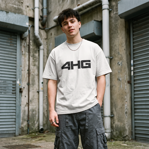 A young man wearing a light gray oversized t-shirt with a bold black '4H6' graphic on the chest, paired with dark gray cargo pants, standing in front of an industrial concrete building with metal roll-up doors.