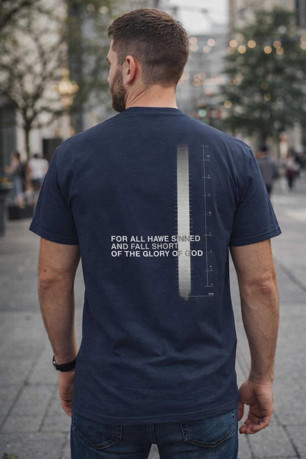 Man wearing a navy blue t-shirt with text and measurement scale on the back, standing on a street.