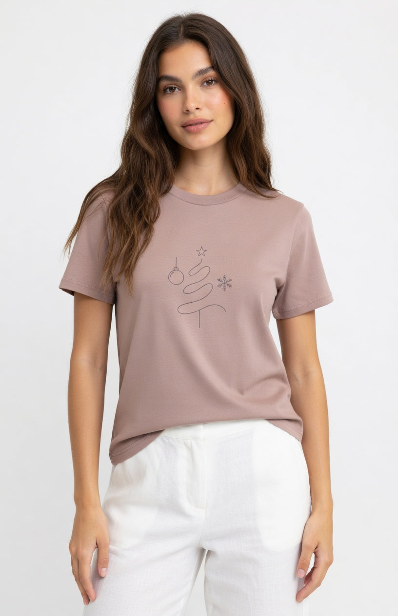 A woman modeling a dusty rose short-sleeve t-shirt with a small black line-art graphic of a tree and stars on the chest, paired with white pants, against a plain white background.