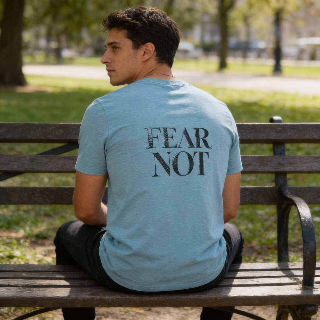Person wearing a blue t-shirt with 'FEAR NOT' on the back, sitting on a park bench.