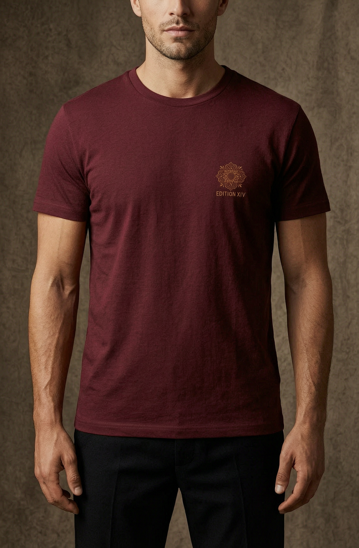 A man wearing a burgundy crewneck t-shirt with a small gold geometric logo and the text 'EDITORIAL' on the left chest, paired with black trousers, set against a textured brown studio backdrop.