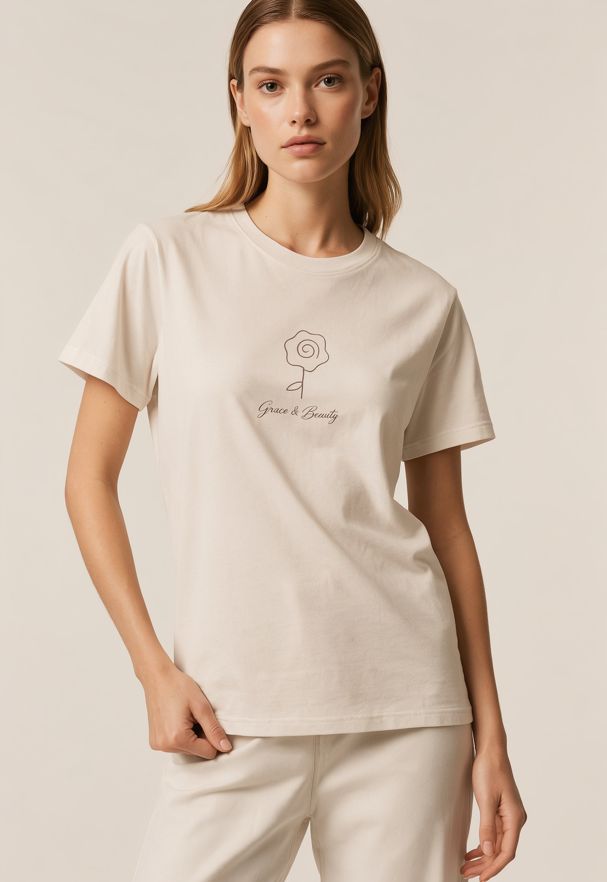 A woman modeling a cream-colored short-sleeve t-shirt with a minimalist line-art flower graphic and the text 'Grace & Beauty' printed on the chest, paired with matching cream pants against a solid beige background.