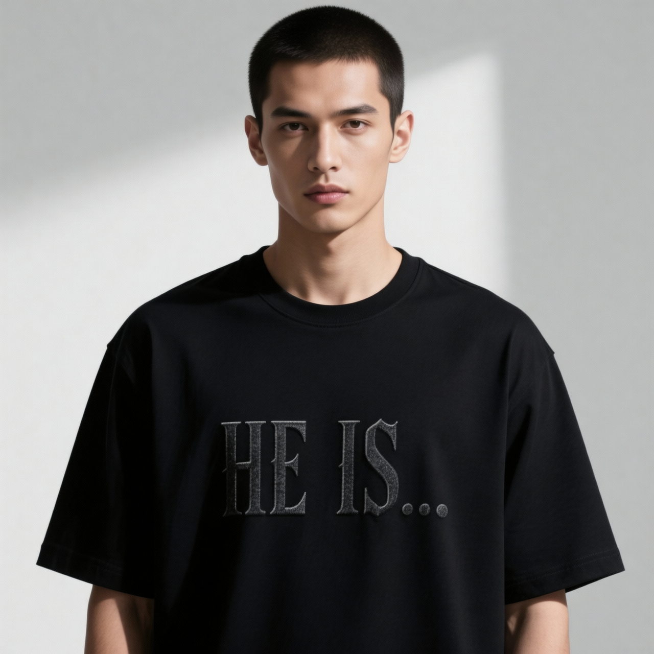 A man wearing a black crewneck t-shirt with 'HE IS.