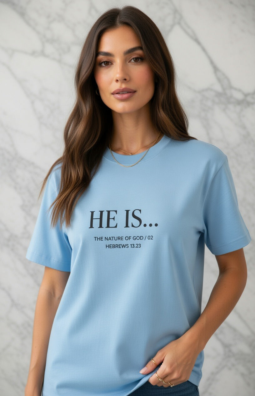 A woman wearing a light blue crewneck t-shirt with the text 'HE IS.