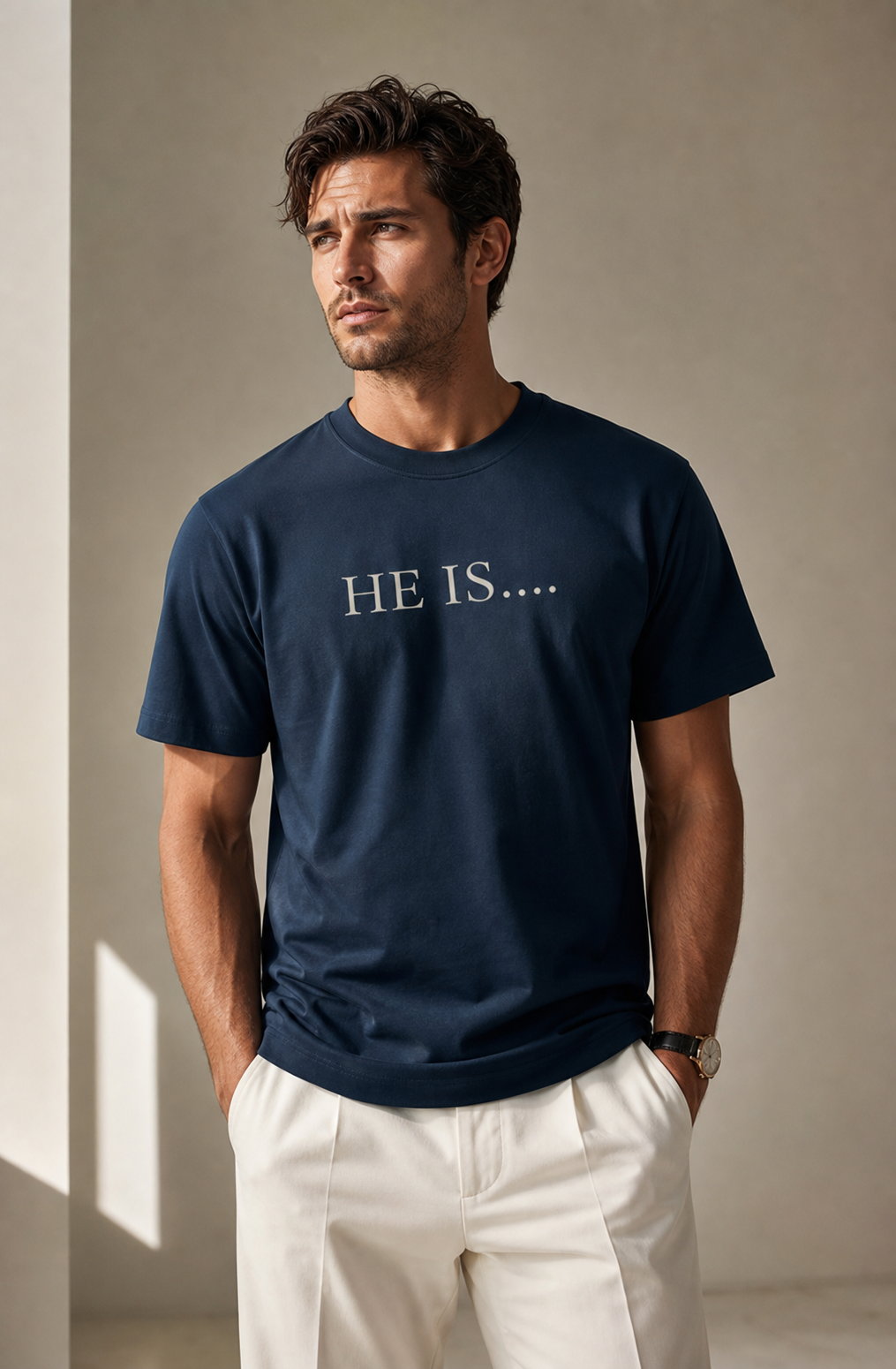 A man wearing a navy blue crewneck t-shirt with the text 'HE IS.