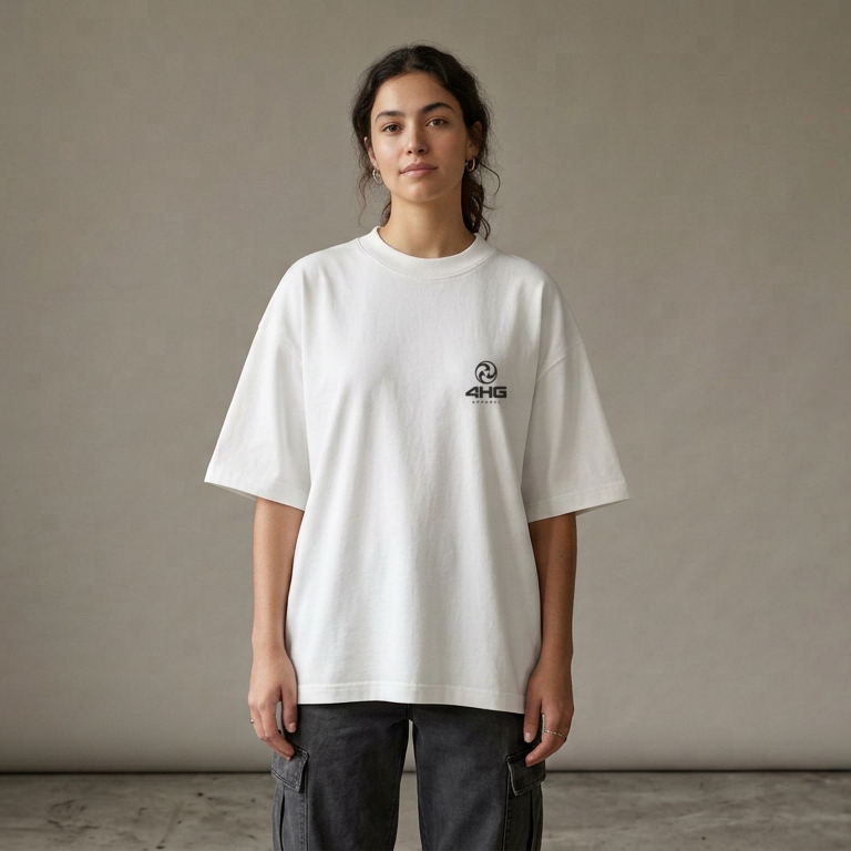 A woman wearing an oversized white t-shirt with a small black graphic on the left chest, paired with dark gray cargo pants, standing against a neutral gray wall.