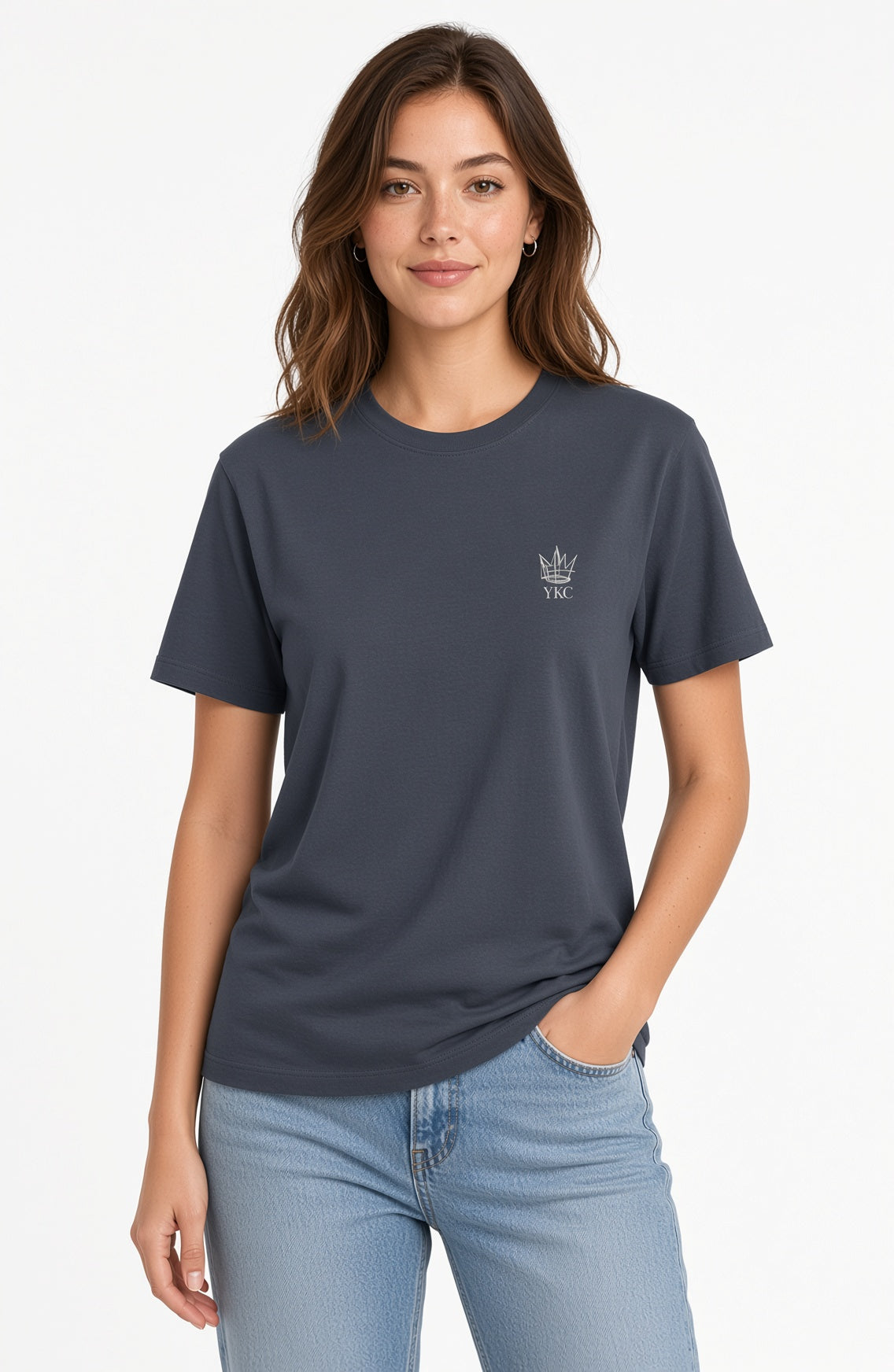 A woman wearing a dark slate blue crewneck t-shirt with a small white embroidered crown logo on the left chest, paired with light blue jeans, against a plain white background.