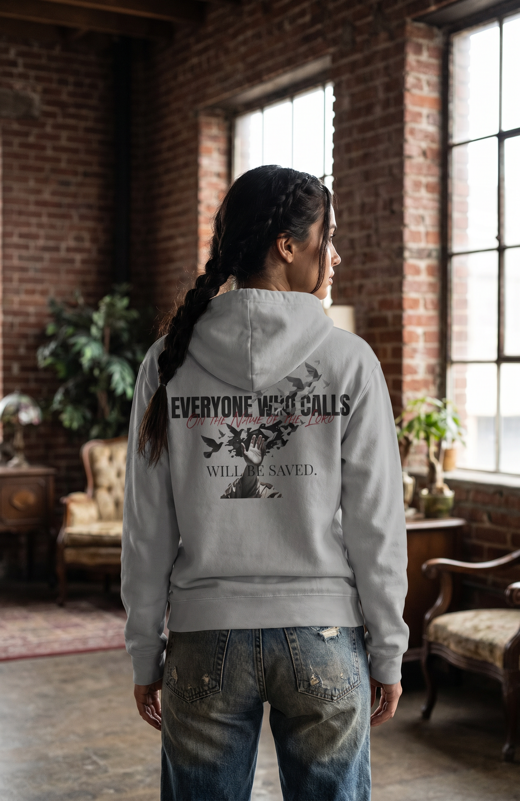 Person wearing a hoodie with text and graphics in a room with brick walls and large windows.