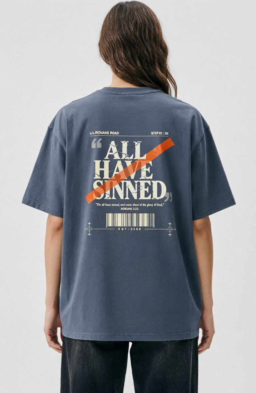 A person shown from the back wearing an oversized slate blue graphic T-shirt with a large white text print reading 'ALL HAVE SINNED' crossed out with an orange diagonal line, paired with dark jeans against a light gray studio background.
