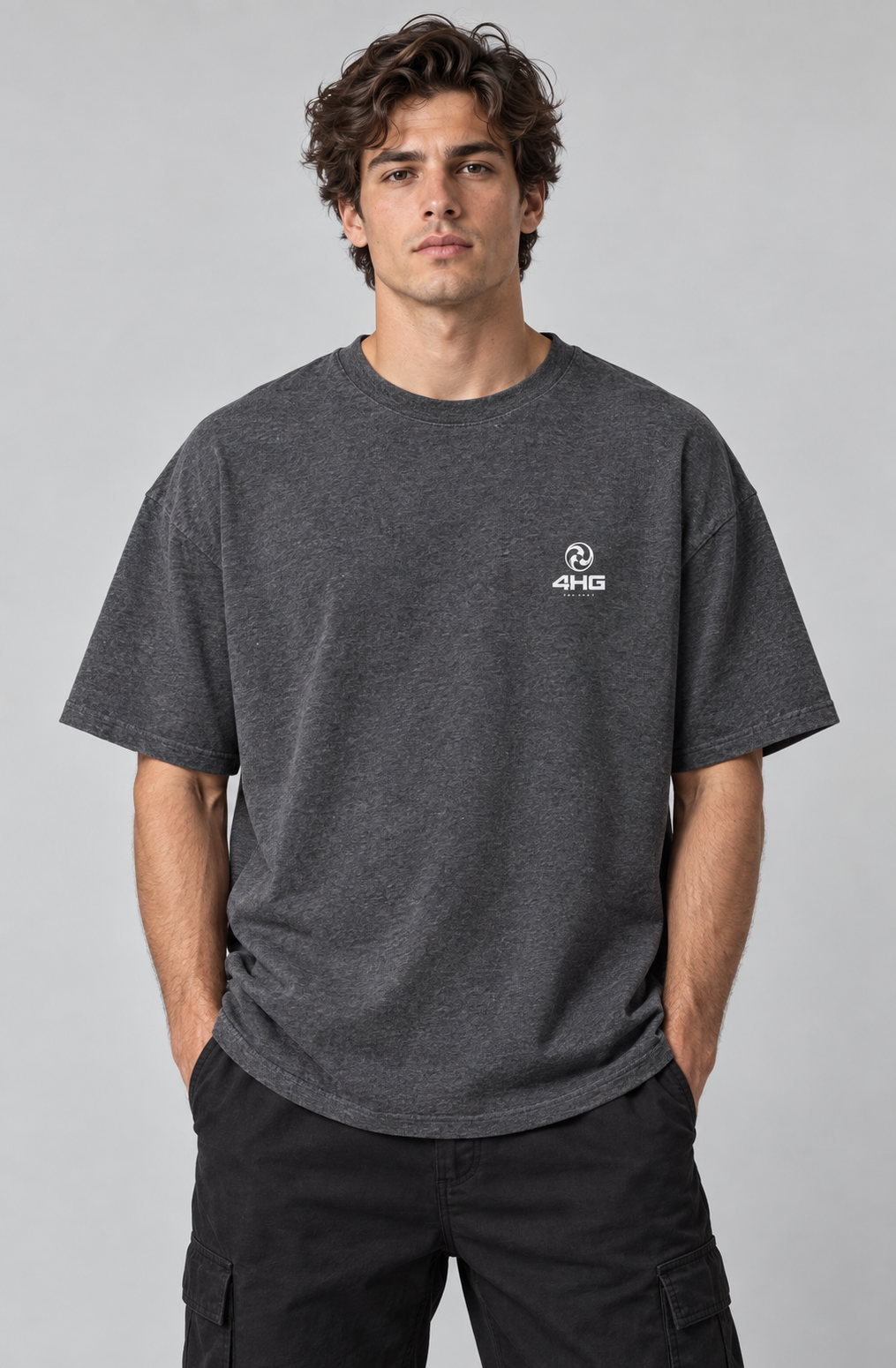 A man wearing a dark heather gray short-sleeve t-shirt with a small white 4HG logo on the left chest, paired with black cargo pants, against a solid gray studio background.