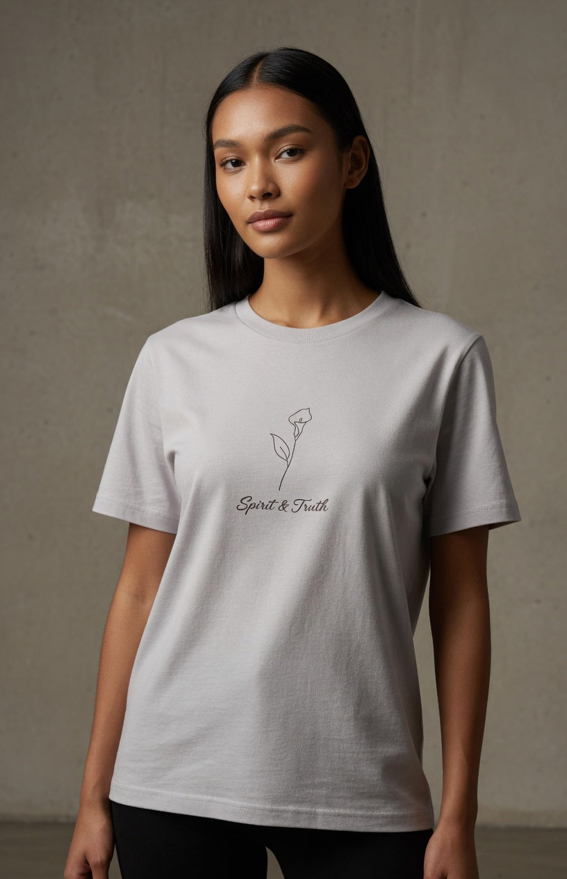 A woman modeling a light gray crewneck t-shirt with a small black line-art rose and the words 'Spirit & Truth' printed on the chest, set against a textured gray concrete wall.