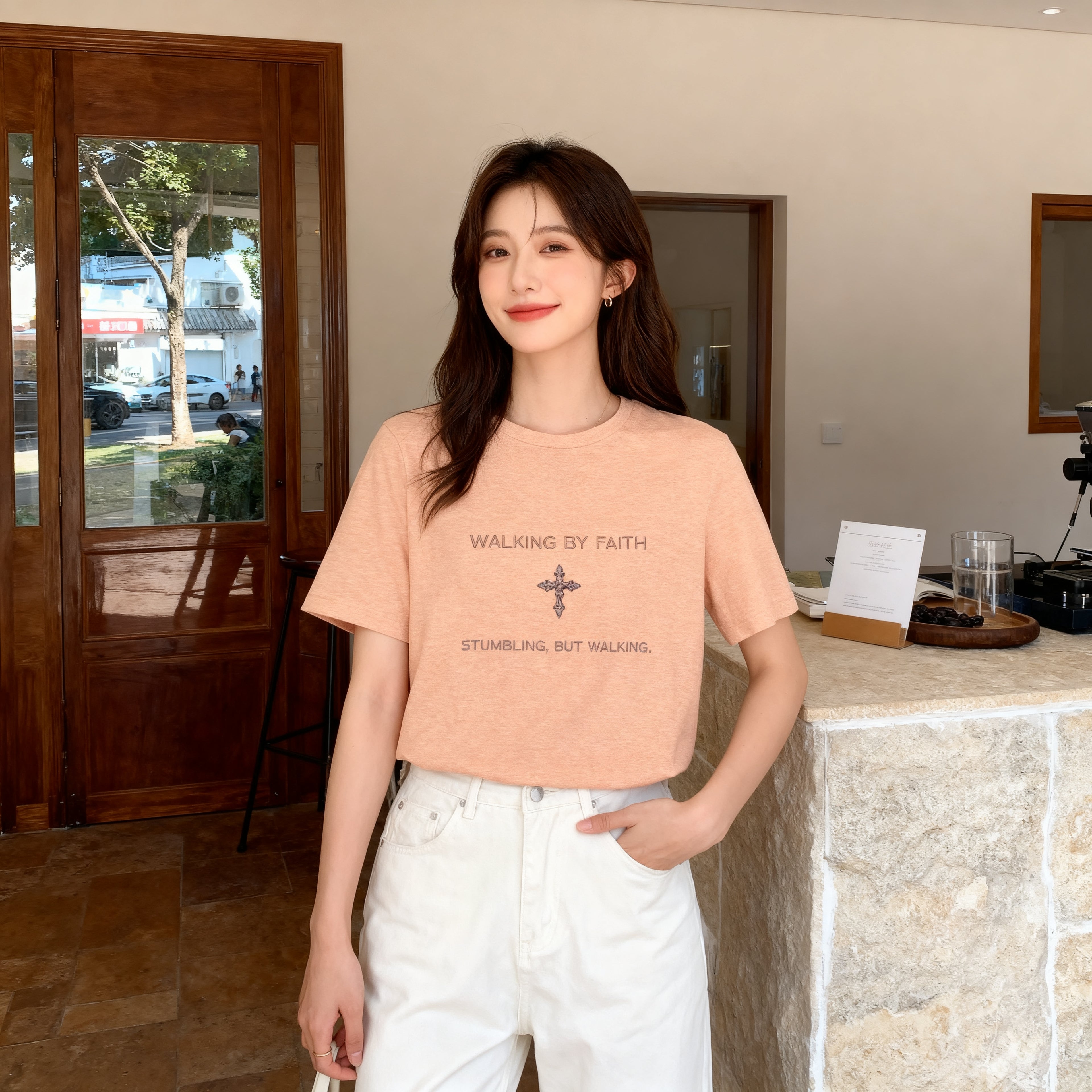 Woman wearing a peach t-shirt with text and a cross symbol indoors.