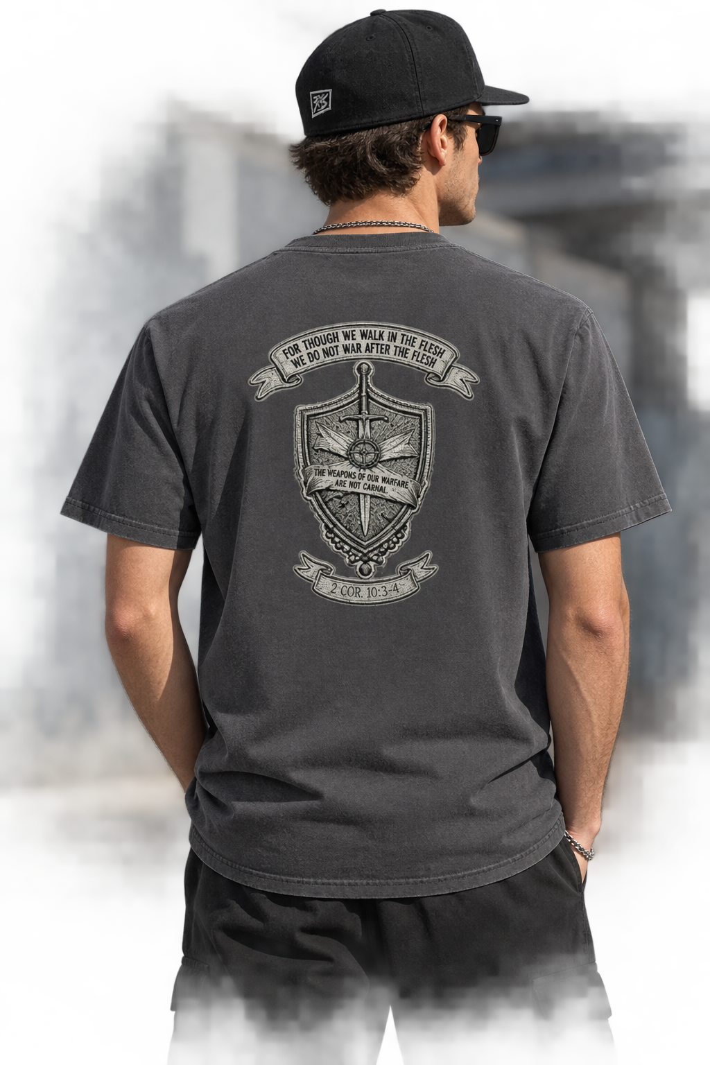 A man wearing a black baseball cap and a faded black t-shirt, viewed from behind to show a large graphic print on the back. The graphic features a military-style crest with a sword, shield, and banner.