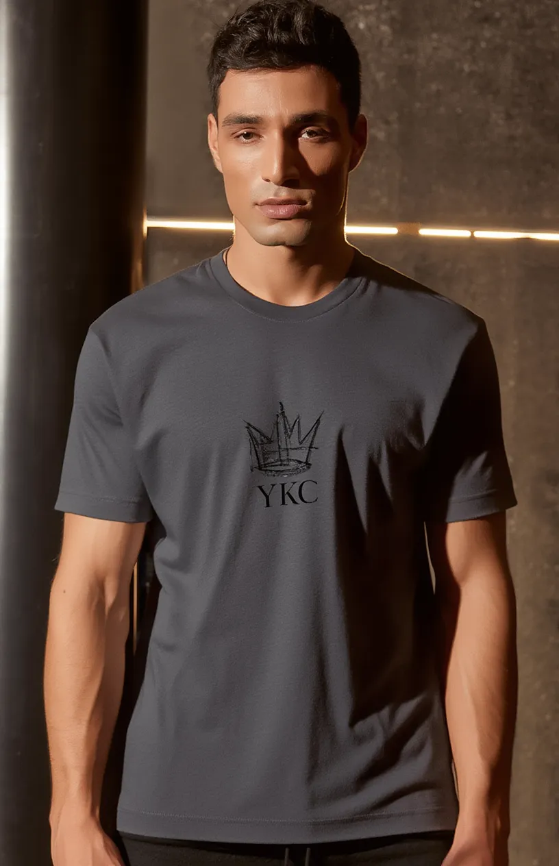Man wearing a dark gray t-shirt with a logo and text, standing against a dark background.